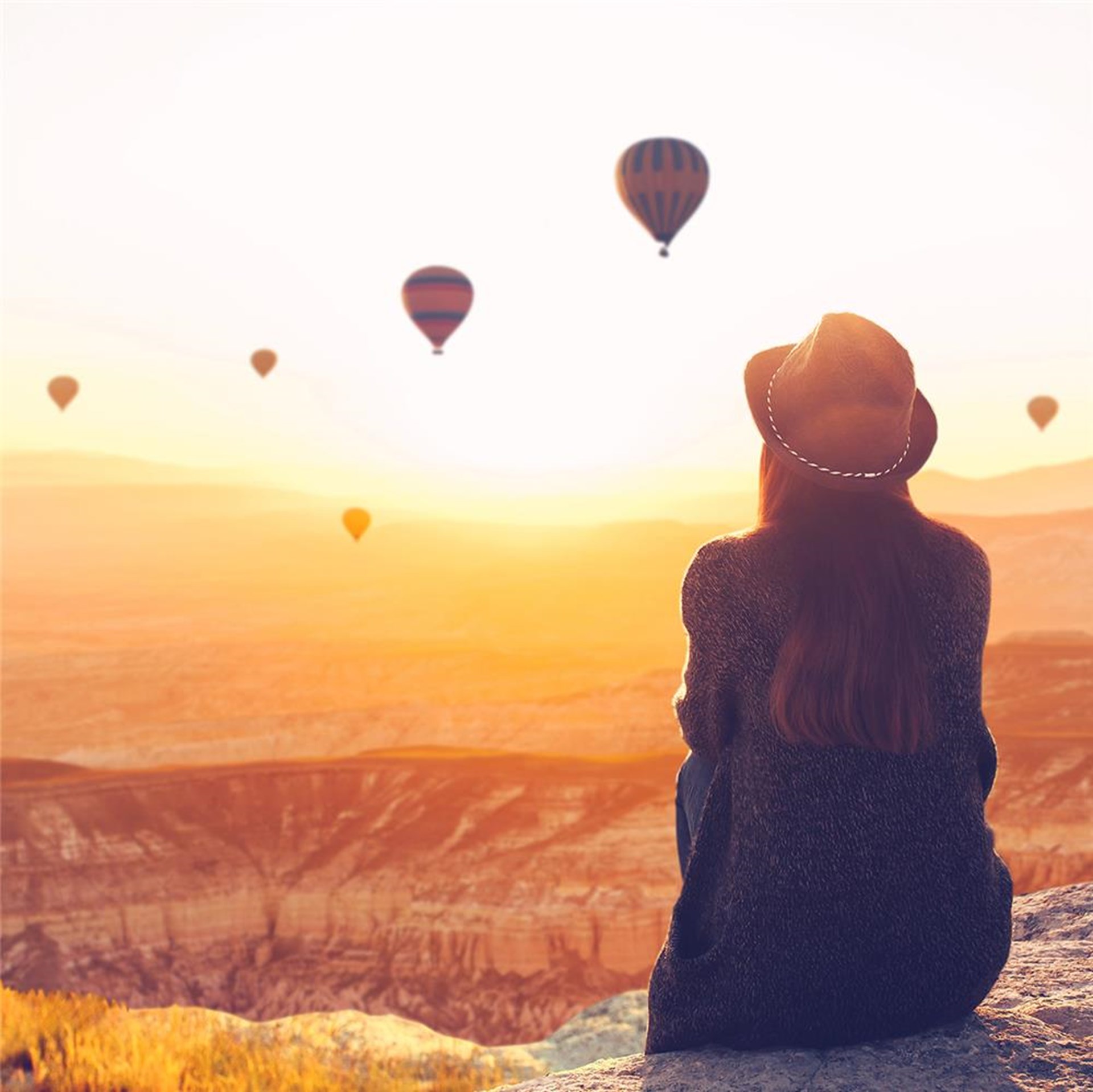 Frau sitzt auf einen Felsen und betrachtet Heißluftballons